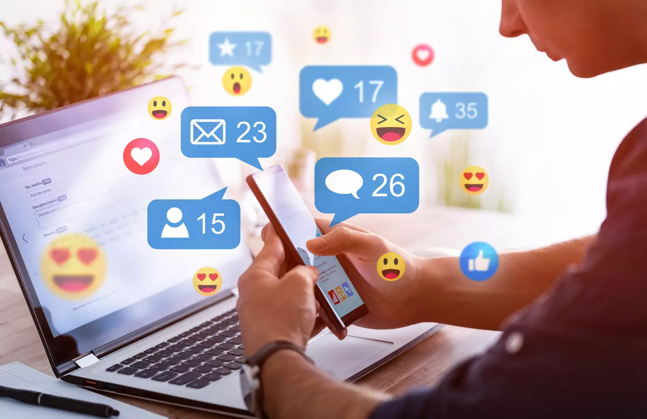 social-media-emojis-and-like-comment-icons-as-person-uses-their-phone-and-laptop