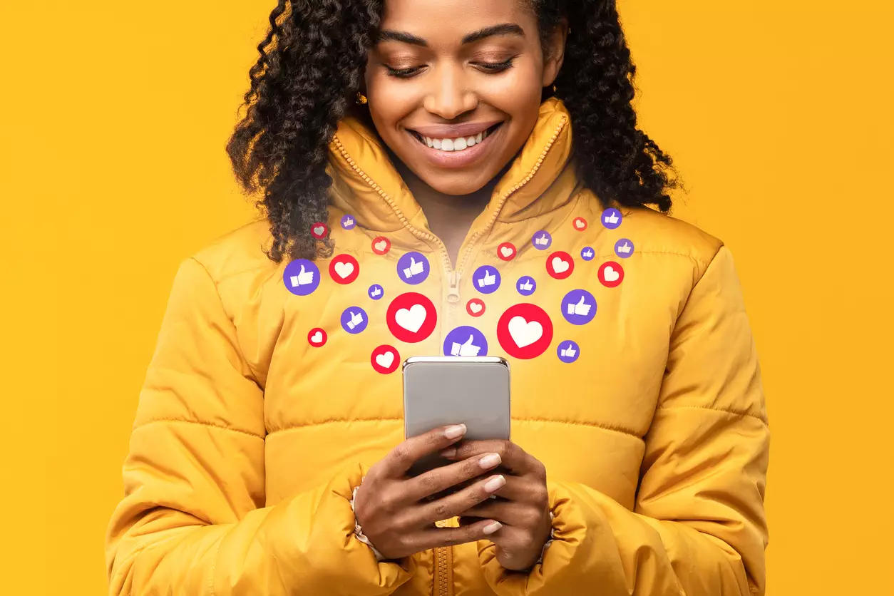 Happy-Black-Woman-Holding-Smartphone-With-Like-Buttons-Yellow-Background